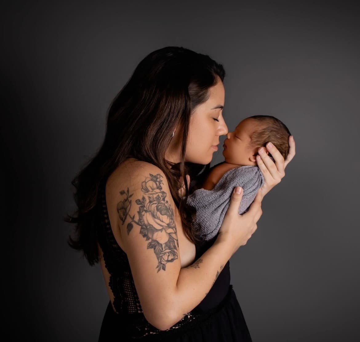 Woman holding and kissing a newborn against a dark studio background